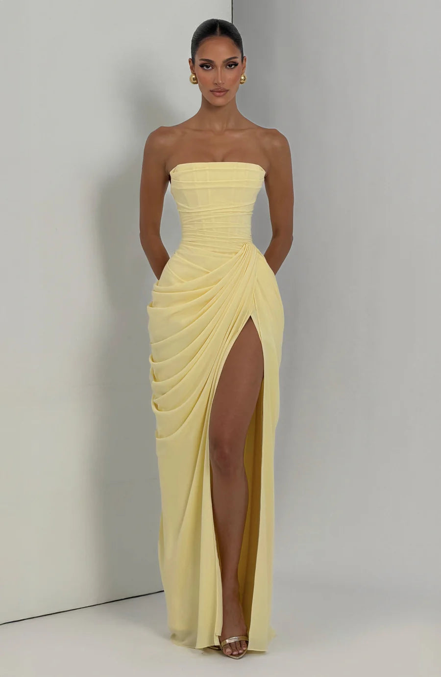 Full-length yellow ruched maxi dress with strapless neckline and side slit, shown in studio corner