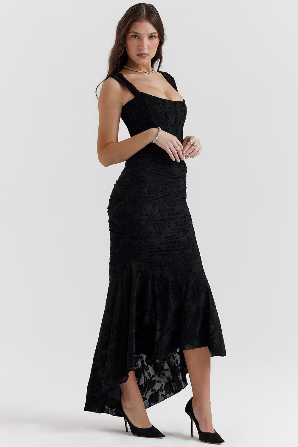 Angled side view of black corset midi dress showing structured bodice, ruching, and high-low skirt