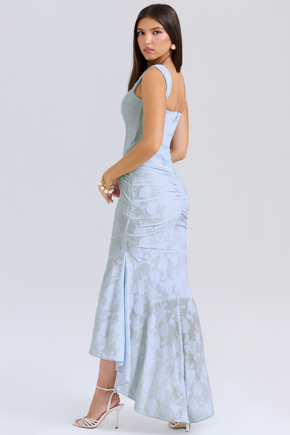 Side view of light blue corset midi dress showing fitted bodice, wide straps, ruched hip and high-low hem