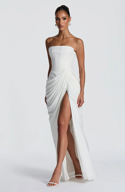 Angled front view of white ruched maxi dress with wrap drape, high slit, and straight neckline