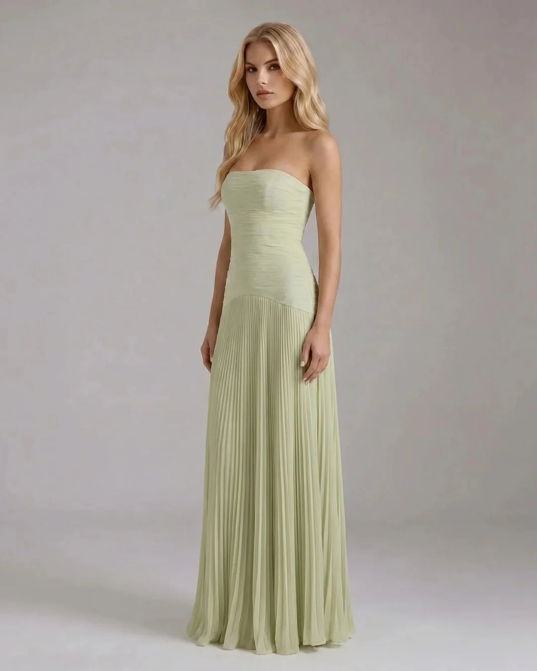 Three-quarter view of sage green strapless maxi dress with fitted bodice and pleated skirt