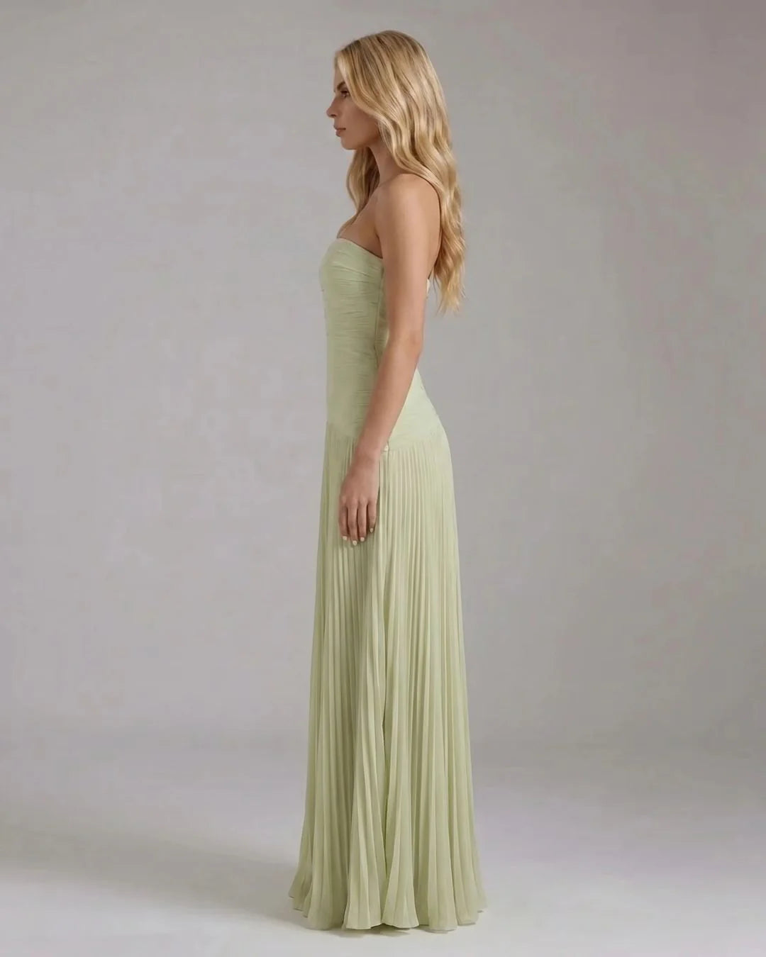 Side profile of light green strapless maxi dress, smooth bodice with flowing pleated skirt