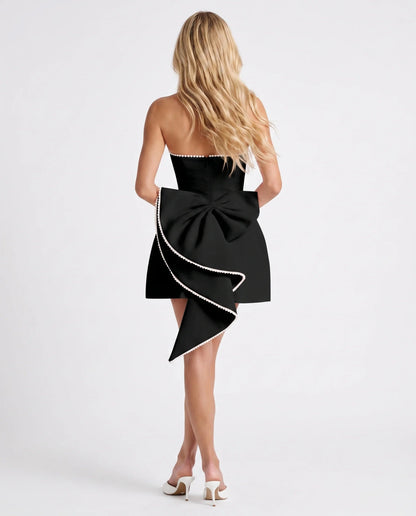 Back view of black mini dress with oversized bow and pearl-edged asymmetric draped train
