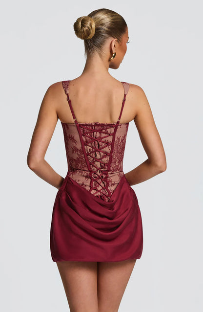 Back view burgundy lace corset mini dress with lace-up corset detail, adjustable straps, and draped skirt