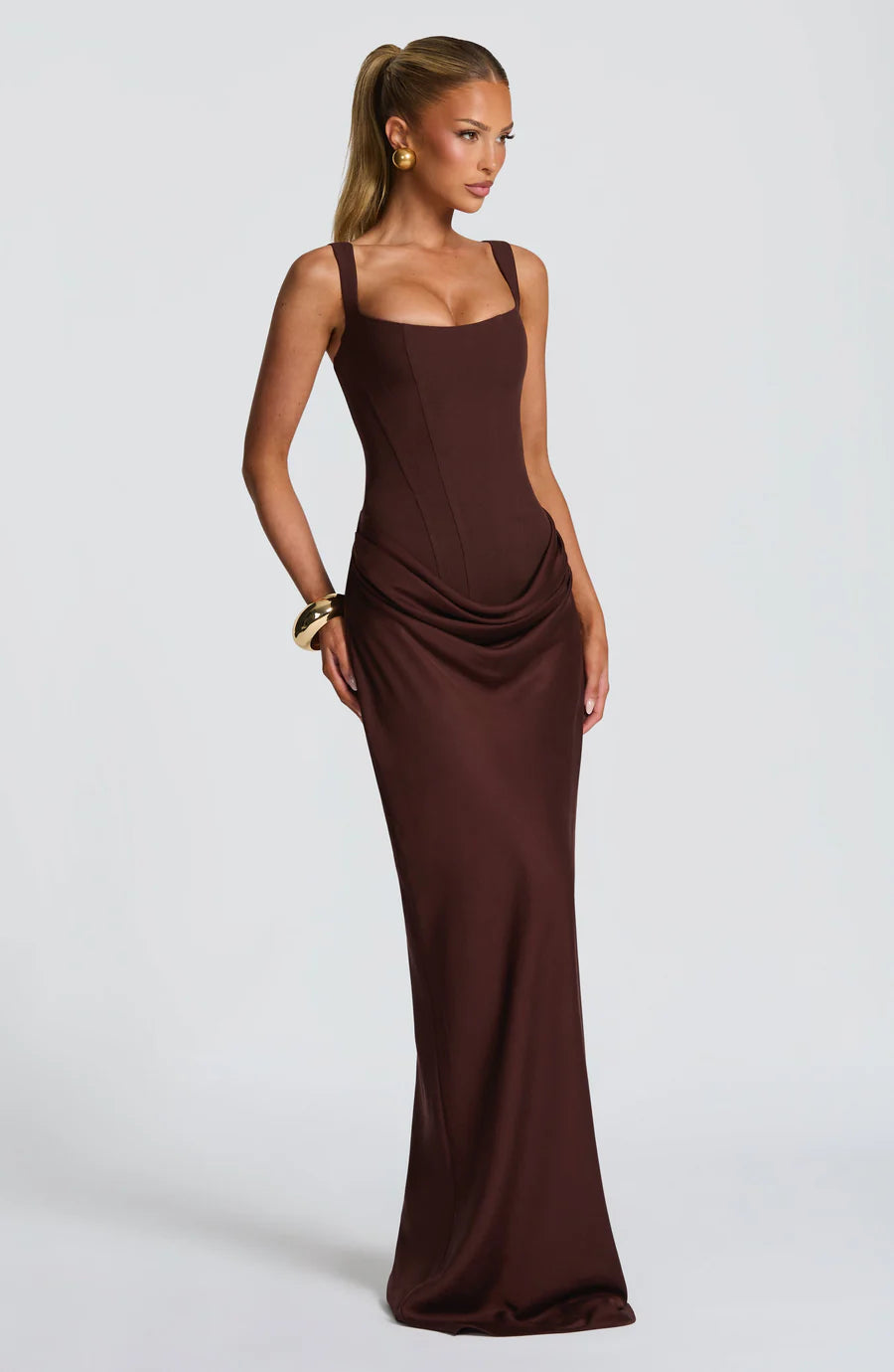 Three-quarter view of brown maxi dress featuring sculpted bodice seams and draped hip detail