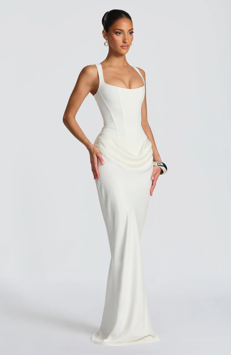Angled view of white maxi dress featuring fitted bodice, hip drape detailing and long straight skirt